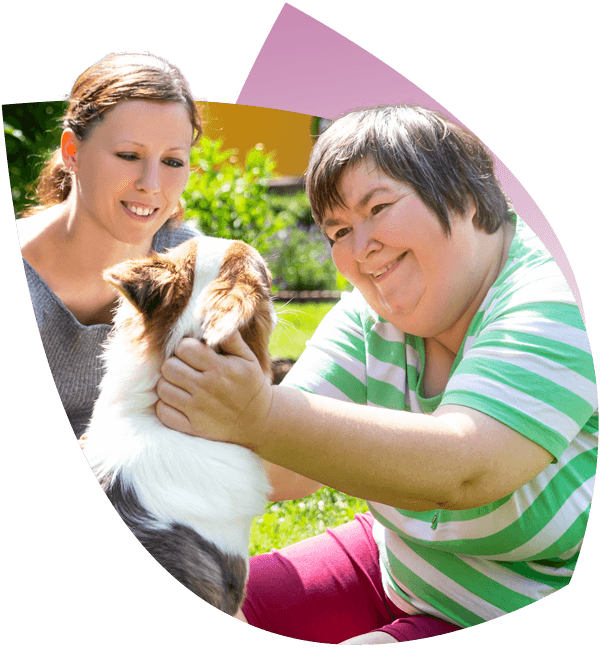 An NDIS Participant enjoys playing with a dog outdoors, assisted by a worker booked from NDIS Rostering Software.