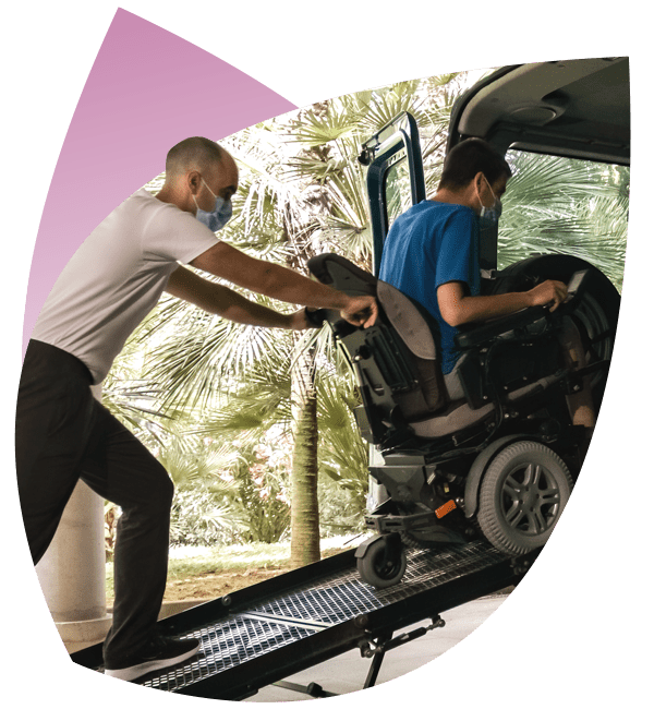 A Support Worker, booked using NDIS Travel Software, is helping an NDIS Participant in a wheelchair to get into a car.